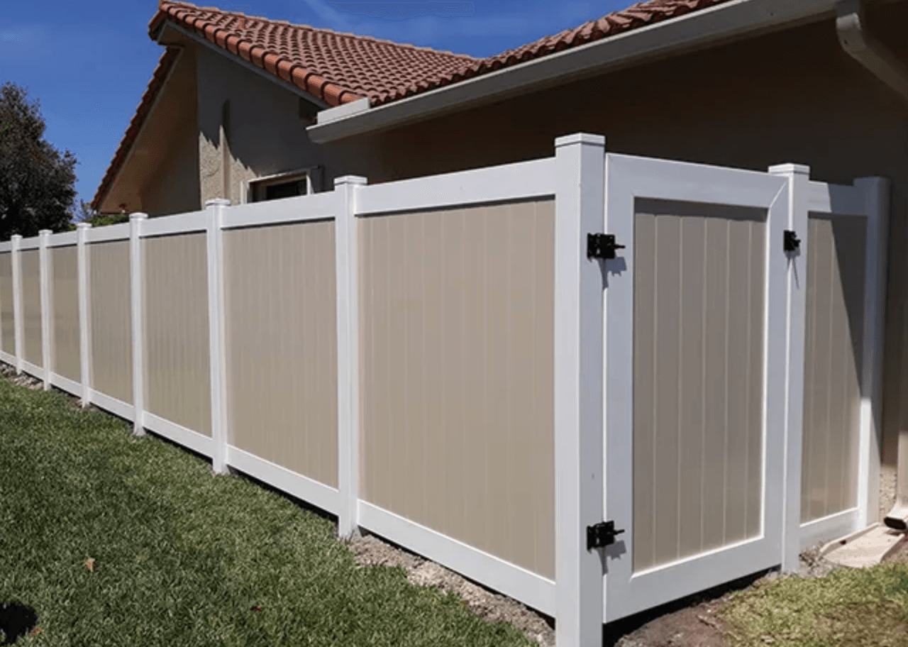 A tan vinyl fence with white border and gate around a home.