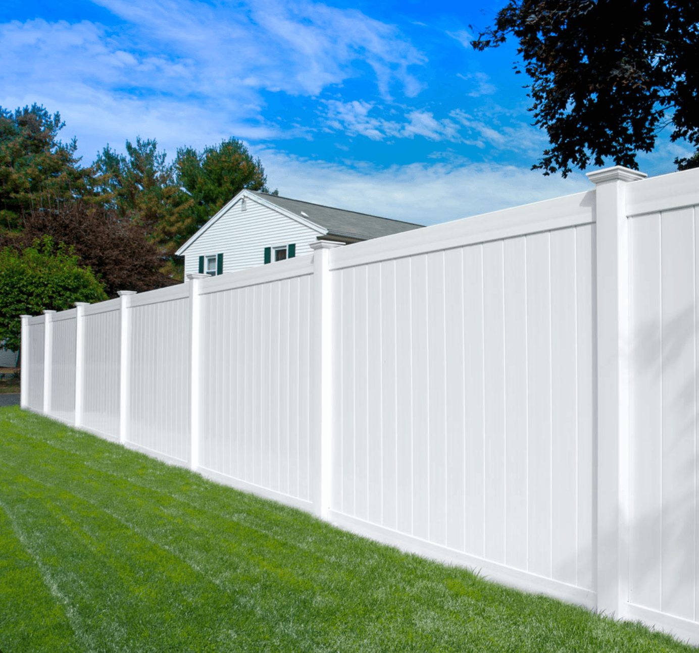 White vinyl fencing panels with green grass below and a white house in the background.